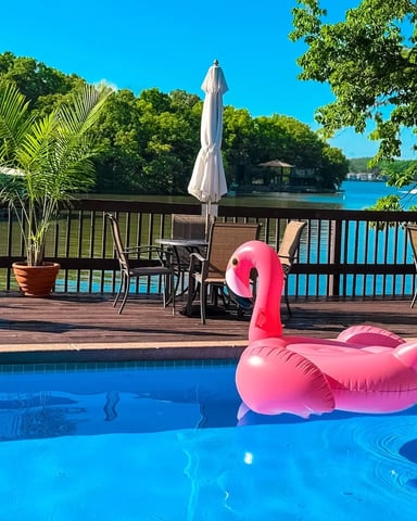 Pool with pink flamingo float, wooden deck with lounge chairs and umbrellas, lake view beyond railing