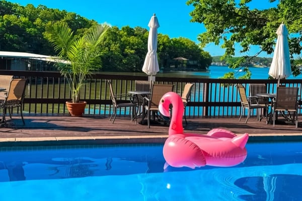 Pink flamingo float in swimming pool with deck, umbrellas, and lake view beyond
