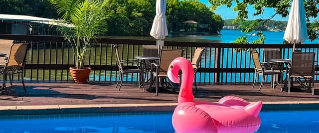Waterfront pool with pink flamingo float, lounge chairs, umbrellas, and lake view beyond wooden deck
